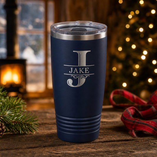 Navy 20 oz tumbler laser engraved with a monogram and the name Jake, on a rustic table with Christmas lights